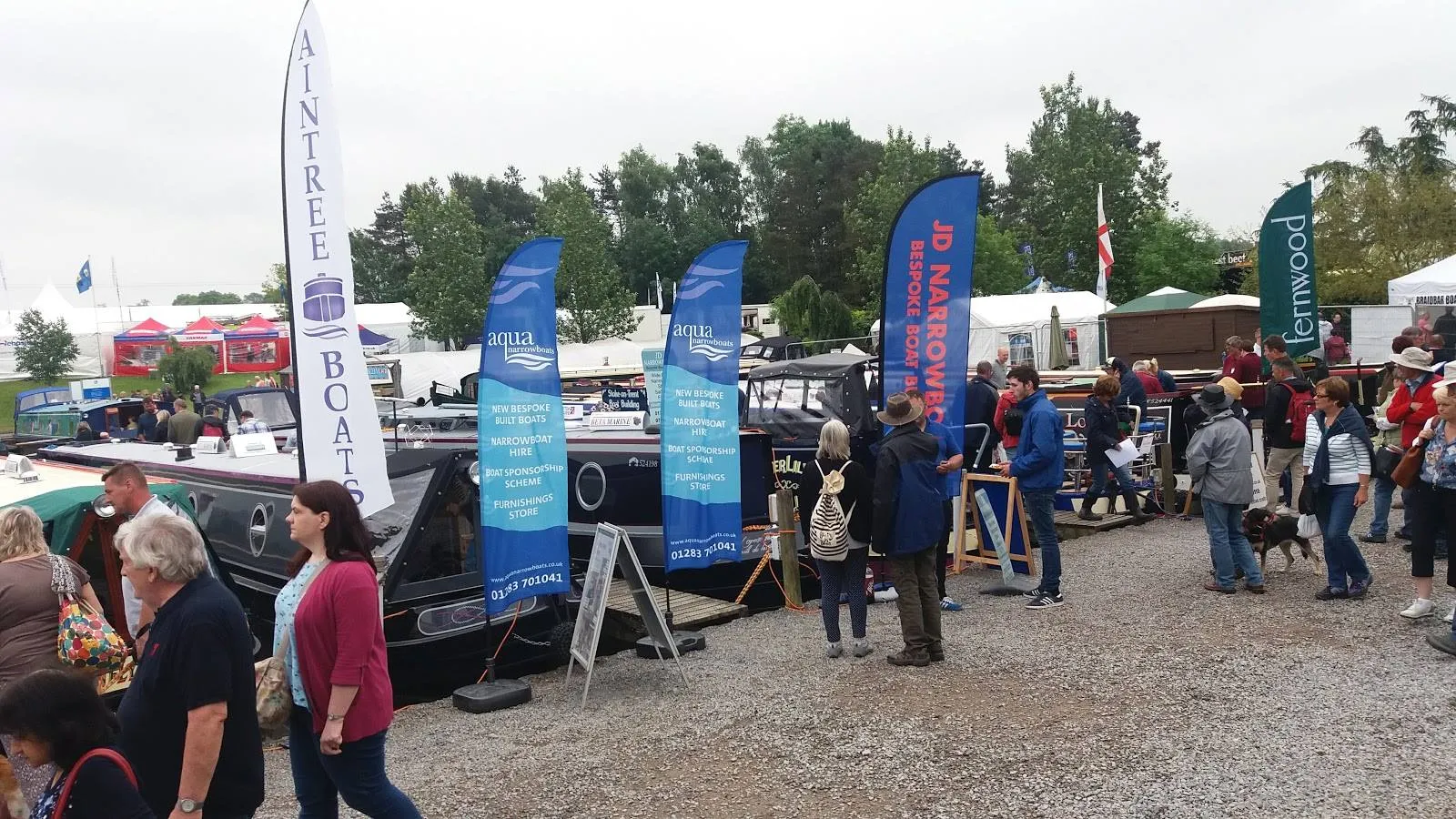 The Aqua Narrowboats stand at the Crick Boat Show, with visitors walking past the moored boats and banners